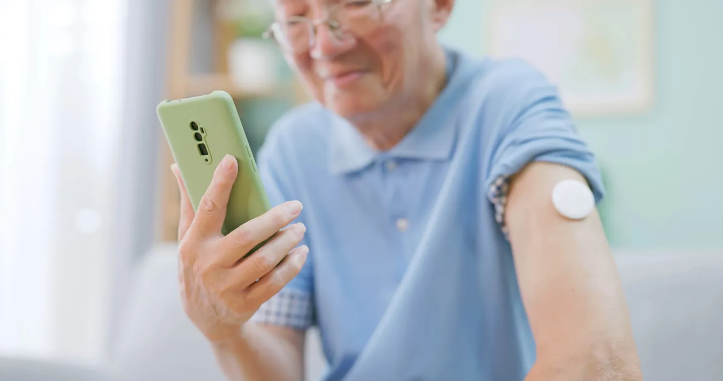 A senior man wearing a Dexcom G7 sensor on his arm, checking his glucose on his phone