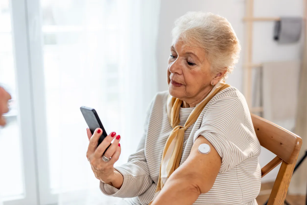 A senior woman wearing a FreeStyle Libre 3 sensor on her arm, checking her glucose on her phone