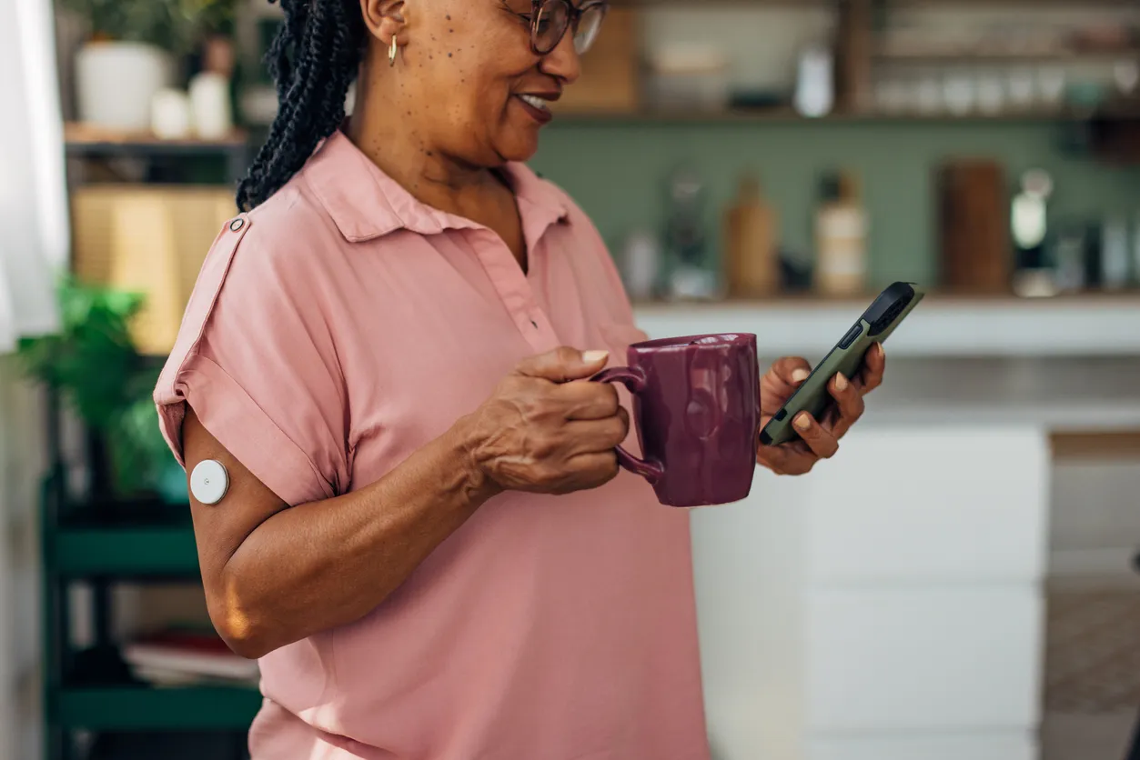 A senior woman wearing a continuous glucose monitor on her arm, checking her glucose on her phone
